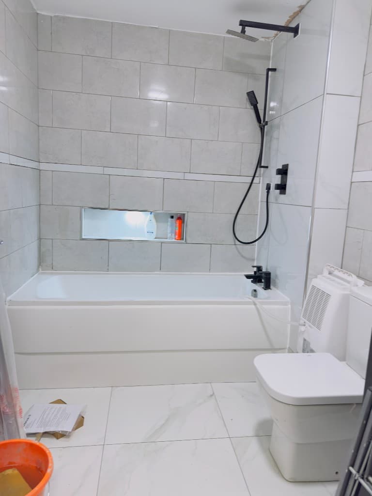 Bathroom with marble-effect tiles, a bath, shower fittings and a close-coupled toilet