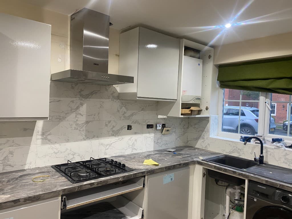 Kitchen installation in progress, with splashback tiling, hob and open cabinets