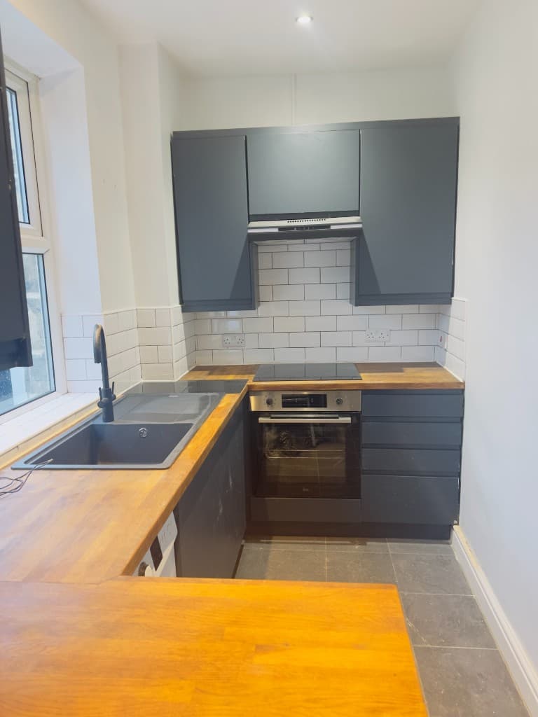 Fitted kitchen with grey cabinets, wooden worktops and a white tiled splashback
