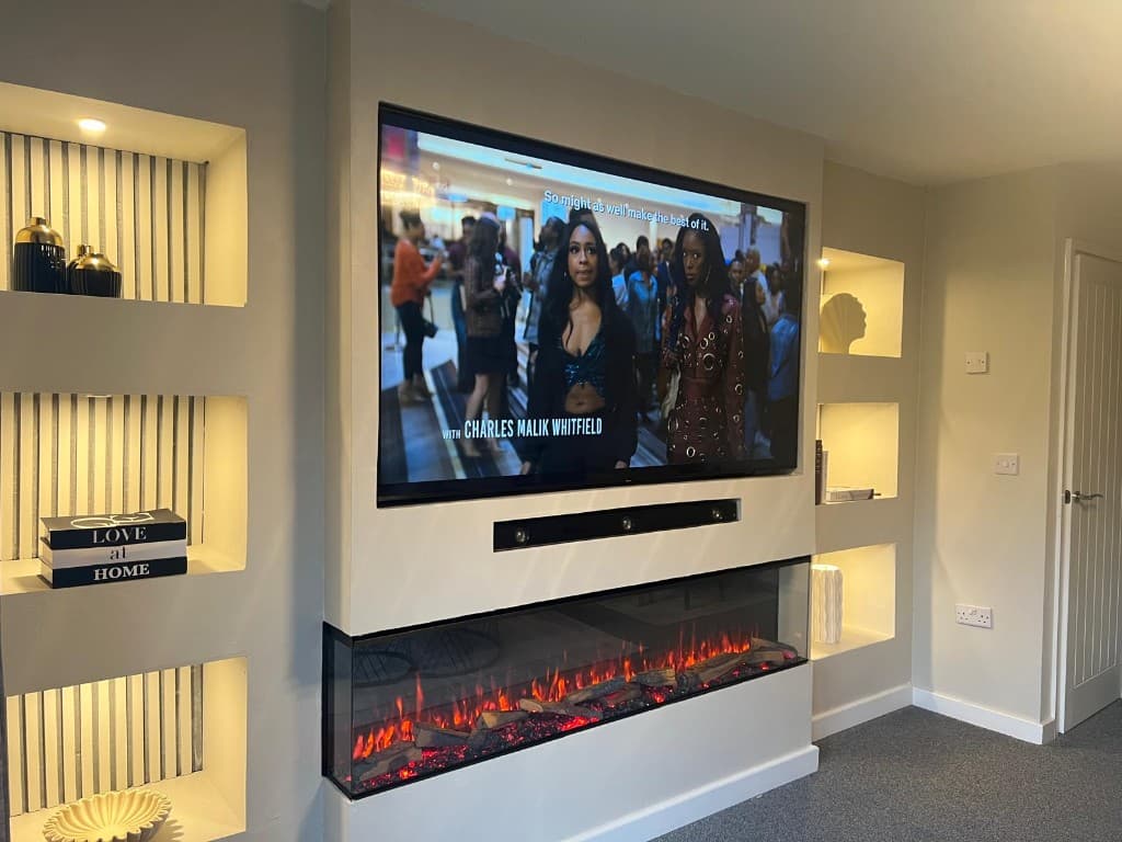 Completed media wall with a wall-mounted television, recessed display niches, integrated lighting and a fireplace