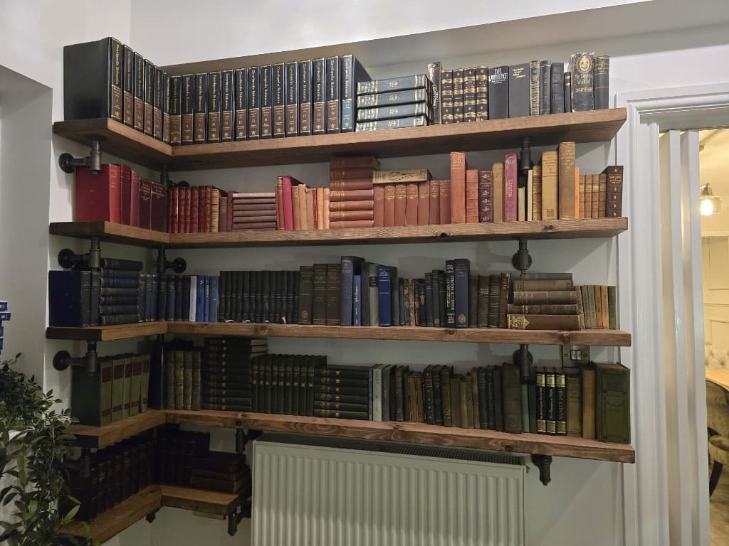 Corner timber shelves on black pipe supports, filled with books